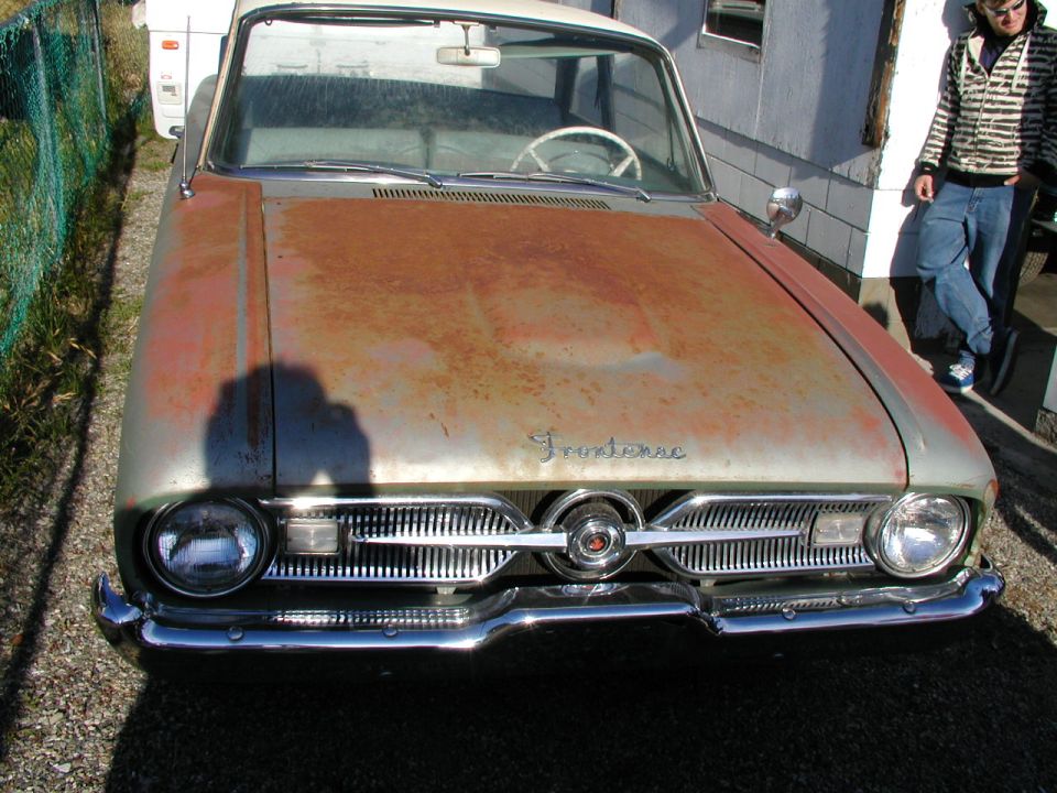 Rusty pale green early-1960s Frontenac sedan front view with chrome grille and hood script badge