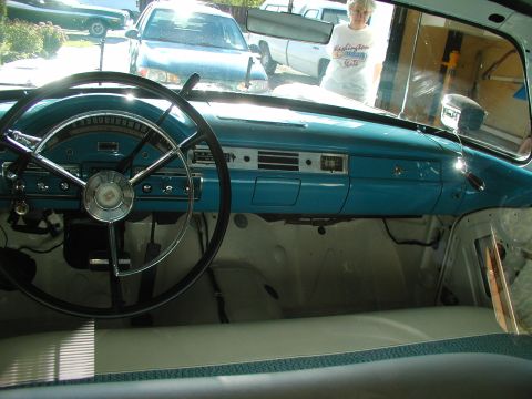 1967 Ford Ranchero - Interior view of a 1957 Ford, its distinctive turquoise dashboard and steering wheel, with other vehicles visible outside.