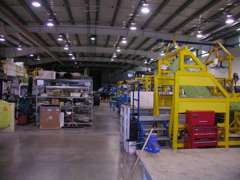 1967 Ford Ranchero - A wide view of a factory floor shows assembly line equipment and storage shelves, with a dark vehicle partially visible.