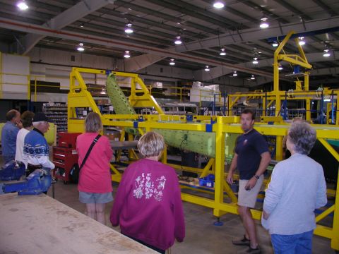 1967 Ford Ranchero - A group of people observe an assembly line in a factory setting with large green components.