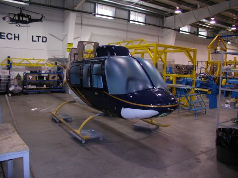 1967 Ford Ranchero - A dark blue helicopter fuselage sits on dollies in a factory setting, surrounded by manufacturing equipment and tools.