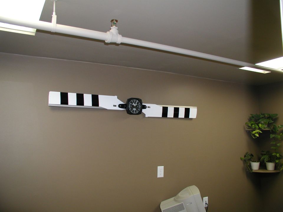 White propeller blade with black stripes and a round gauge mounted on a tan interior wall.