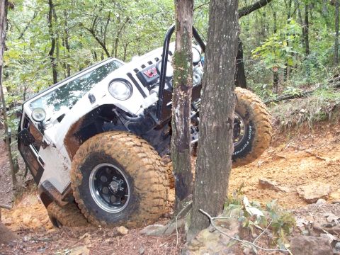 1995 Ford Bronco - Jeep Wrangler navigating a steep, muddy trail in a wooded area.