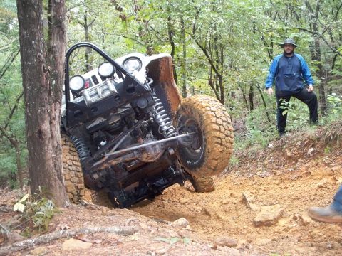 1995 Ford Bronco - An off-road vehicle is stuck on a steep, muddy incline with a person observing the situation.