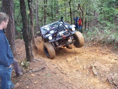 1995 Ford Bronco - A Jeep Wrangler navigates a challenging off-road trail with one wheel significantly elevated.