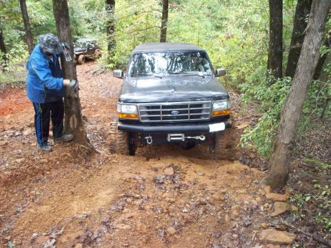 1995 Ford Bronco - Head-on view of a lifted black Ford SUV picking its way through a rocky red-clay trail section, wearing a tube front bumper with a mounted…