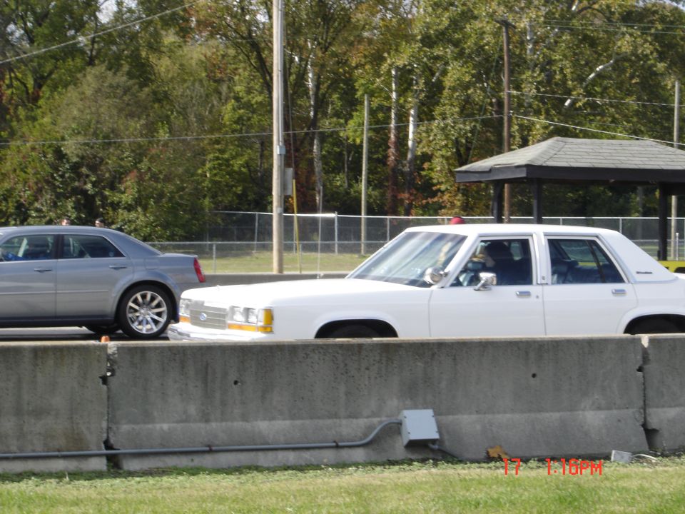 White Ford full-size sedan parked behind concrete barrier, silver sedan behind, outdoor lot