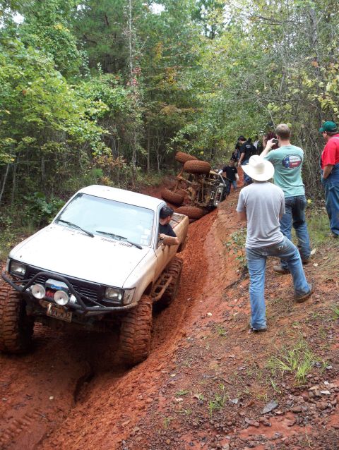 1995 Ford Bronco - Several off-road vehicles are on a muddy trail, with one truck overturned and others attempting to navigate the terrain.