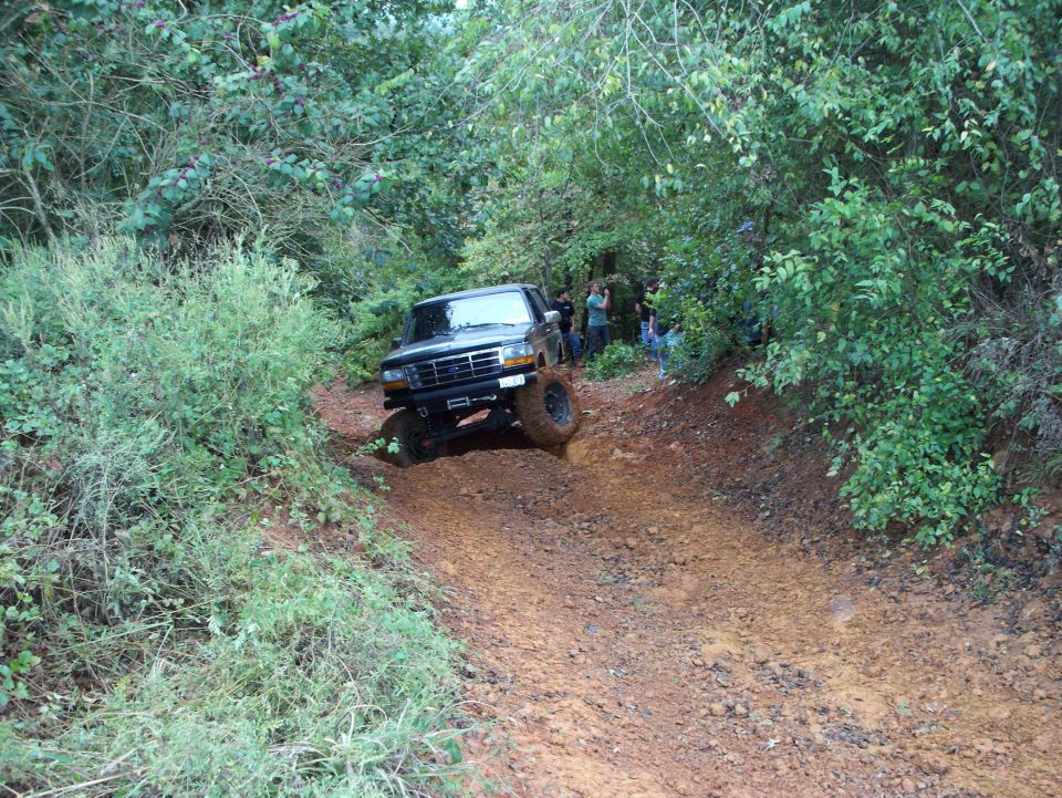 1995 Ford Bronco climbing a steep, muddy trail with trees on either side