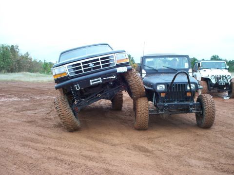1995 Ford Bronco - Modified Ford Bronco and Jeep Wrangler off-roading on a dirt track with other vehicles in the background.