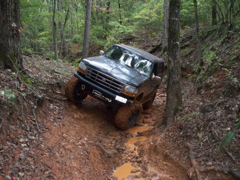 1995 Ford Bronco - A Ford Bronco tackles a challenging muddy incline on a wooded trail.