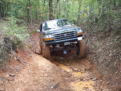 1995 Ford Bronco - A dark-colored Ford Bronco navigates a challenging muddy off-road path.