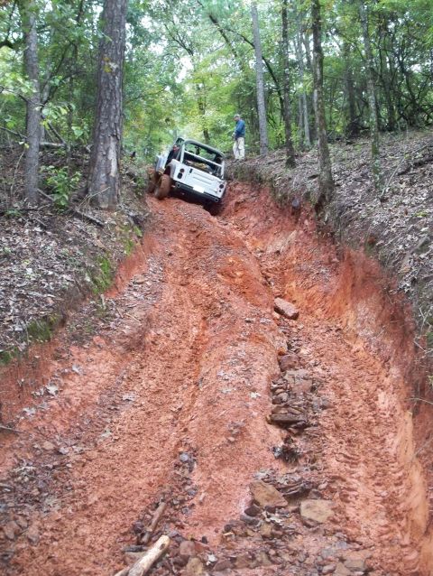 1995 Ford Bronco - Off-road vehicle navigates a challenging muddy incline in a wooded area.
