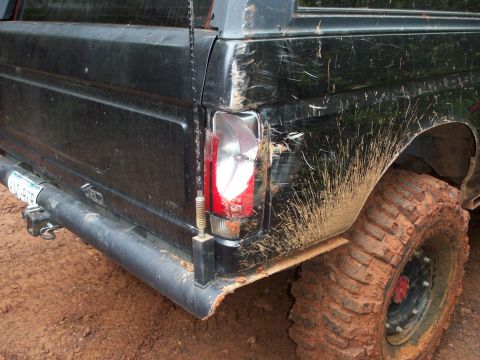 1995 Ford Bronco - Mud-splattered rear of a black SUV with a damaged taillight and off-road tires.