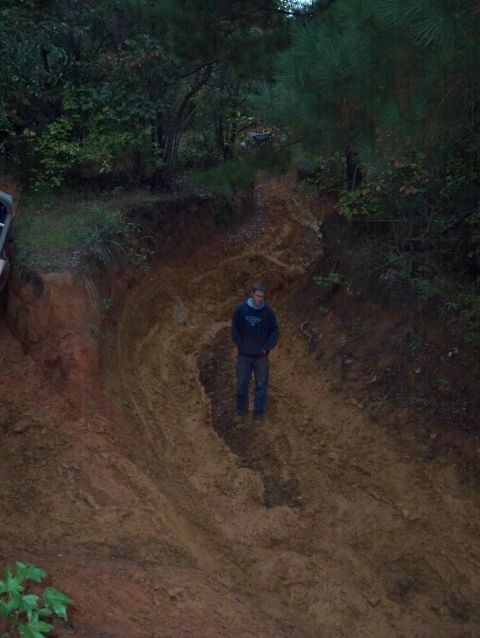 1995 Ford Bronco - A person stands on a steep, muddy incline, surrounded by trees and tire tracks.
