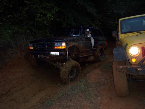 1995 Ford Bronco - Two off-road vehicles navigate a dark, muddy trail at night.