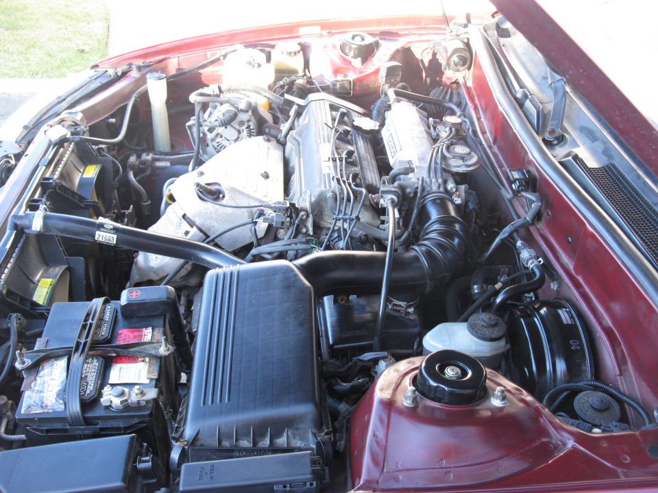 Toyota V6 engine bay with black airbox and battery in a maroon car