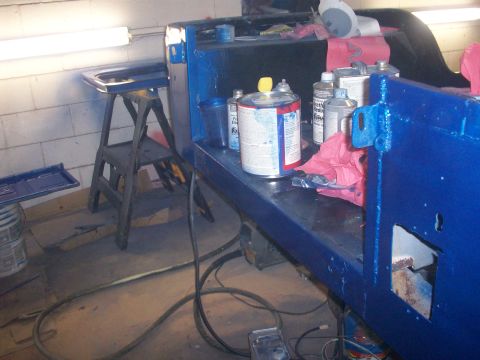 1978 Jeep CJ5 - A blue painted vehicle part sits on a workbench with various paint cans and rags, suggesting a restoration or repair process.
