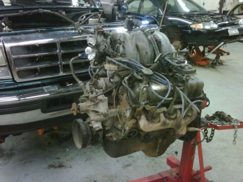 1996 Ford Bronco - Engine removed from a vehicle, with another vehicle in the background also undergoing repairs.