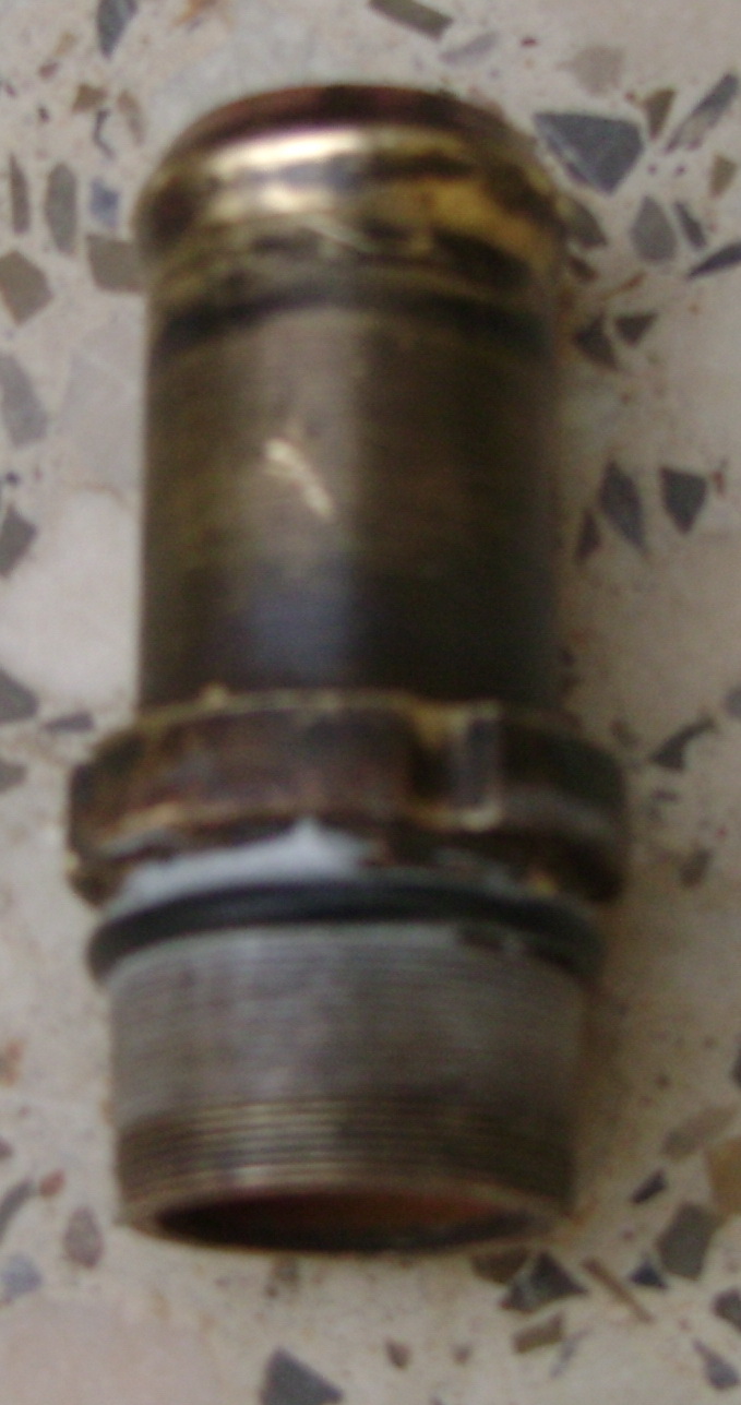 Close-up of a metal pipe fitting with threaded end and a brass-colored top
