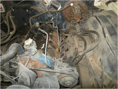 Dirty V8 engine bay of an older vehicle with rusty firewall and components