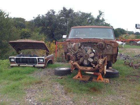 1978 Ford Bronco - Two Ford trucks in a yard, one disassembled for work, the other with its hood open.