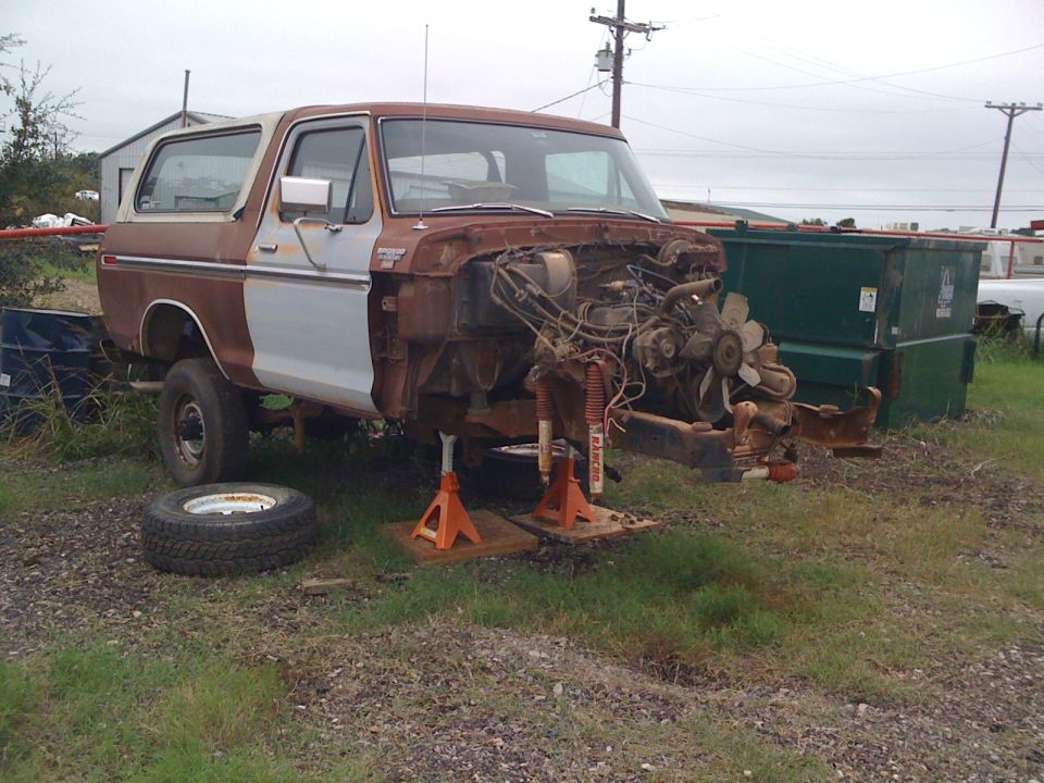 Rusty 1978 Ford Bronco with front end removed, sitting on jack stands. Spare tire is on the ground
