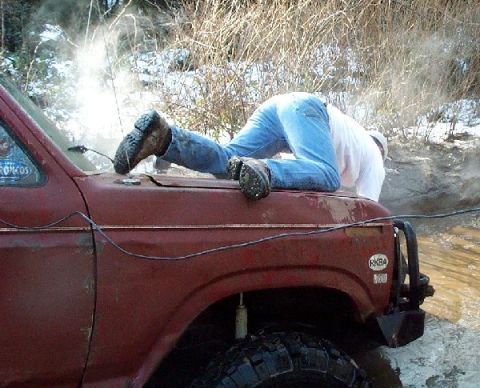 1982 Ford Bronco - A person works on the hood of a red 1982 Ford Bronco, with steam or smoke rising.