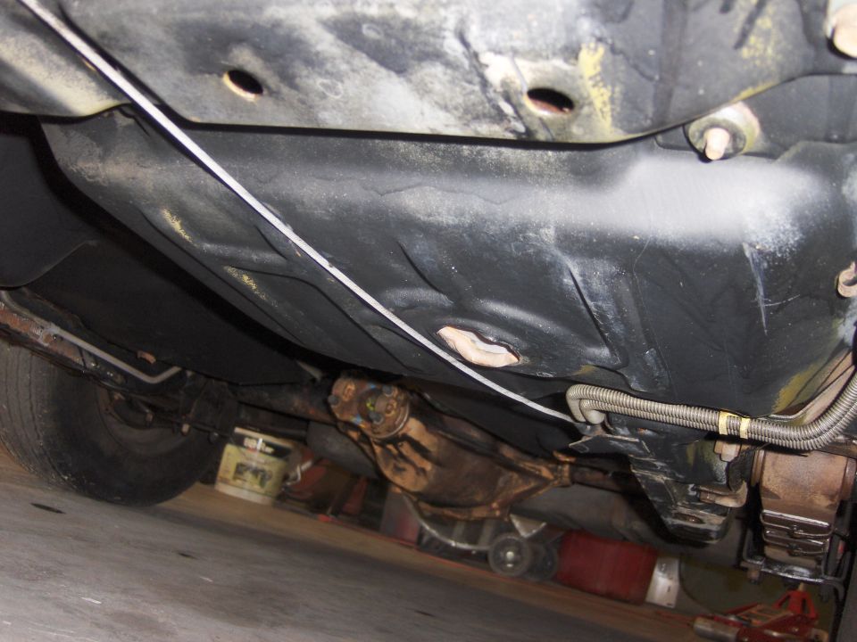 Underside view of a car, showing the fuel tank, driveshaft, and rear axle