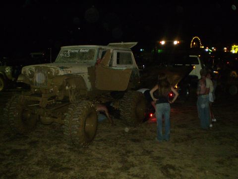 2005 Ford Excursion - A heavily modified Jeep Wrangler, covered in mud, sits in a field at night with people around it.