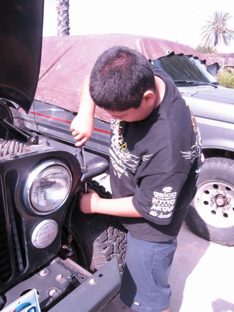 1986 Ford Bronco - A person works on the front of a Jeep Wrangler, with another vehicle partially visible in the background.