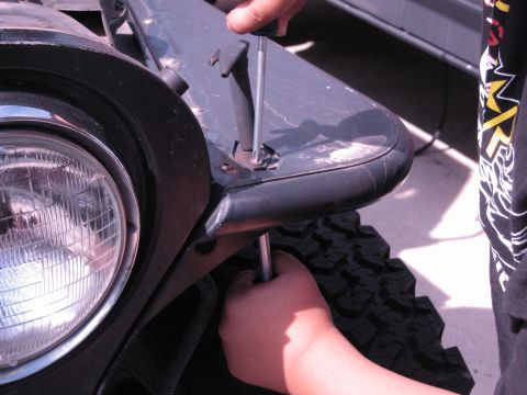 1986 Ford Bronco - A person is using a screwdriver to work on the fender of a Jeep Wrangler near the headlight.