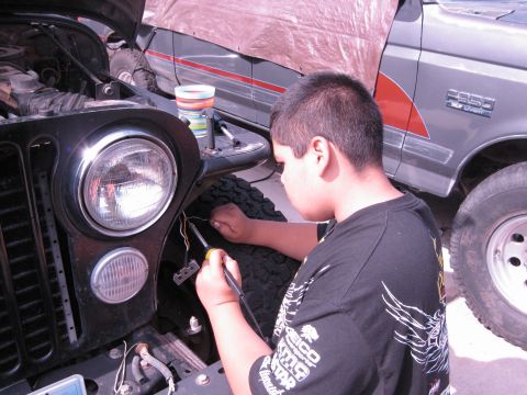 1986 Ford Bronco - A person works on the front end of a black Jeep, with a Ford F-350 visible behind it.