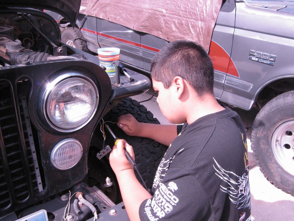 Black Jeep front end with wiring exposed; Ford F-350 in background