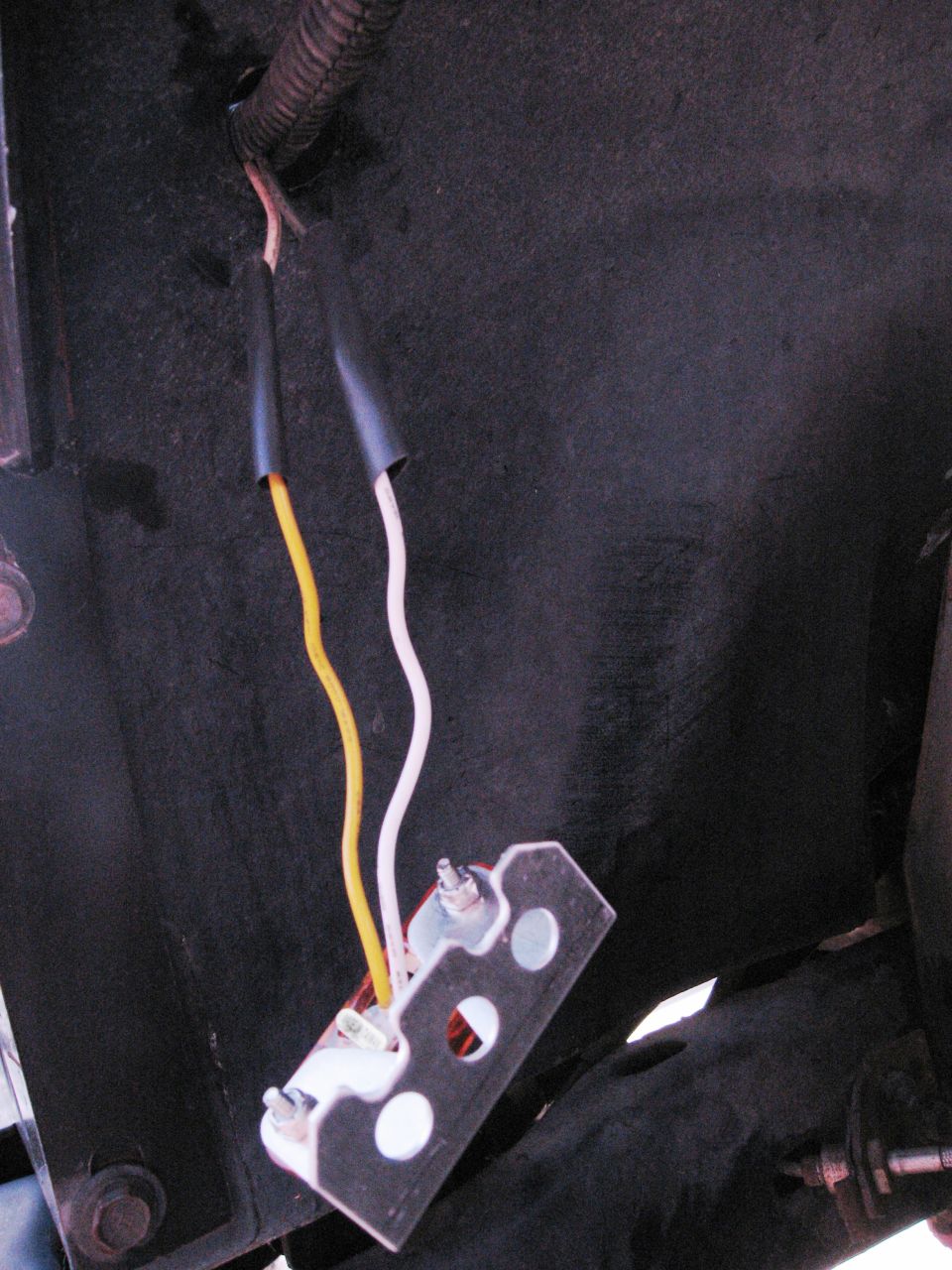 Close-up of a vehicle's electrical connector with yellow and white wires leading to a metal bracket