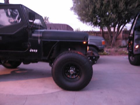 1986 Ford Bronco - A black Jeep CJ-7 is parked on a paved surface, with another vehicle visible to its right.
