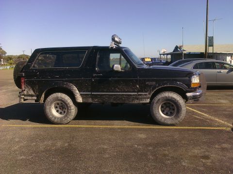 1993 Ford Bronco - This black 1993 Ford Bronco is equipped with off-road tires and a light bar, seen parked next to another vehicle.