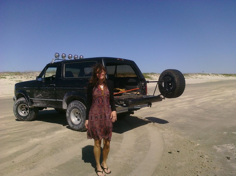 Black Ford Bronco with spare tire on rear, light bar on roof, on a sandy beach