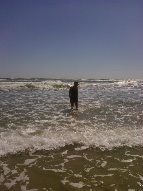 1993 Ford Bronco - A person stands in the ocean as waves crash around them under a clear blue sky.