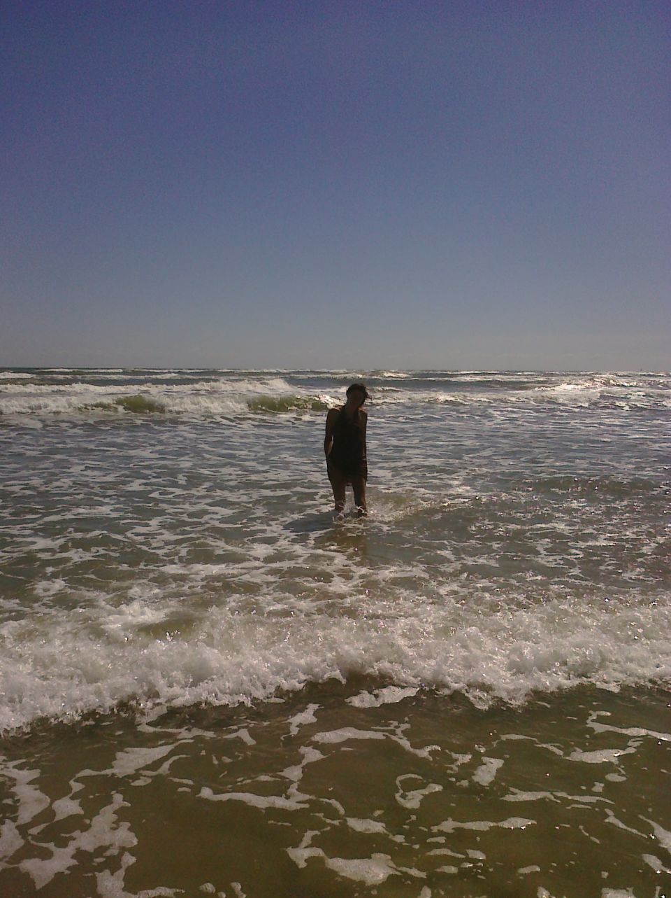 Person standing in ocean waves with whitecaps