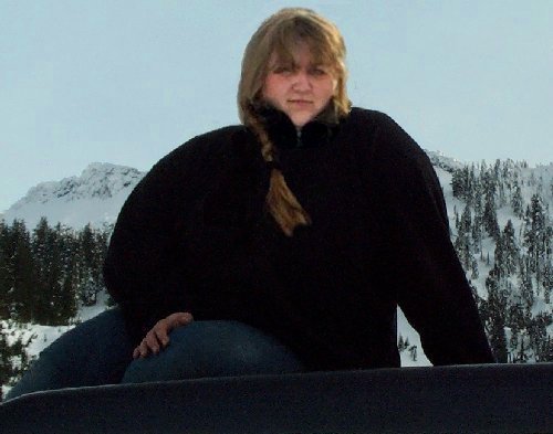 Person in black fleece sitting on a dark vehicle panel with snowy mountains behind