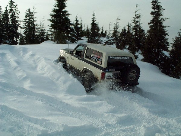 Two-tone Ford Bronco with rear tire carrier plowing through deep snow on a ridge
