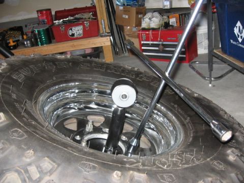 1995 Ford Bronco - A lug wrench and jack are positioned inside a large tire, with tools and toolboxes in the background.