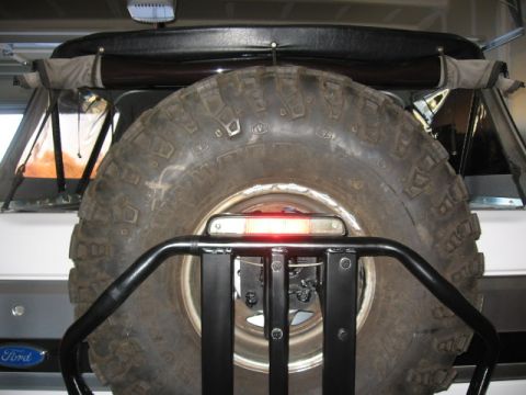 1995 Ford Bronco - Rear view of a vehicle's spare tire carrier with a large tire and a red brake light mounted above it.