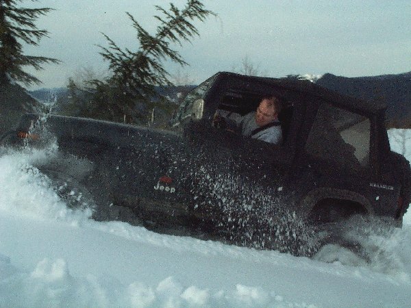 Dark soft-top Jeep Wrangler plowing through deep snow and throwing powder