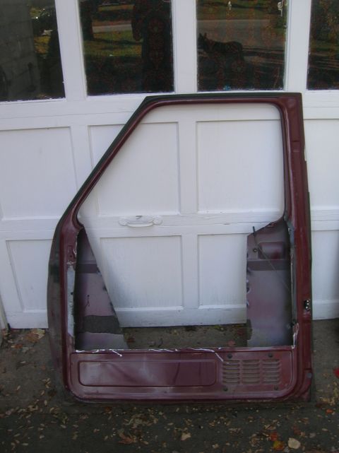 1996 Ford Bronco - Inner-side view of a stripped maroon truck door leaning against a white garage door, with the outer skin largely cut away to expose the doo…