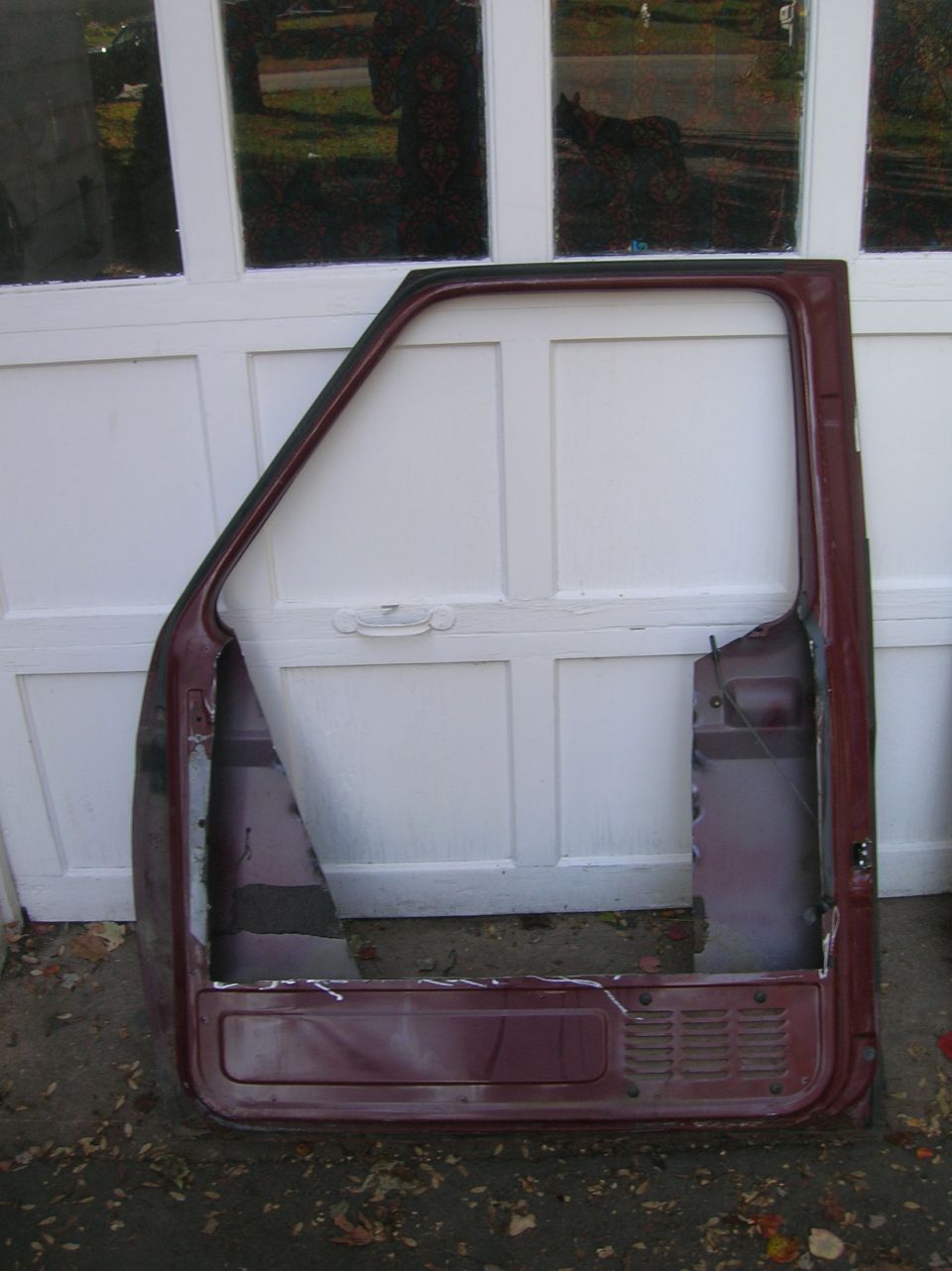 Inner view of a stripped maroon truck door with cut-away skin leaning on a garage door