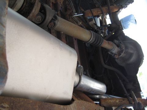 1995 Ford Bronco - The undercarriage of a vehicle reveals a muffler and driveshaft, with visible rust on the metal parts.