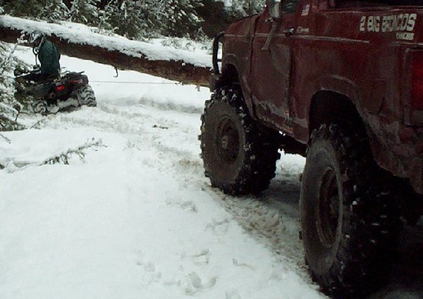 Red lifted Ford Bronco on mud tires in the snow with an ATV rider behind it