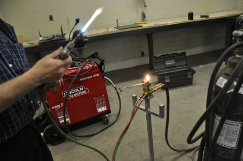 1996 Ford Bronco - A person uses a welding torch connected to a Lincoln Electric Power MIG welder, with gas cylinders nearby in a workshop setting.